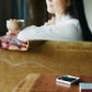 a hibi incense match is burning on its pad, a girl is drinking tea in the background