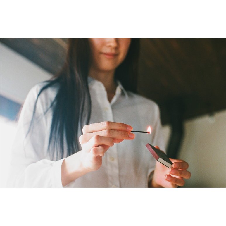 a girl in white shirt lighting a hibi incense match