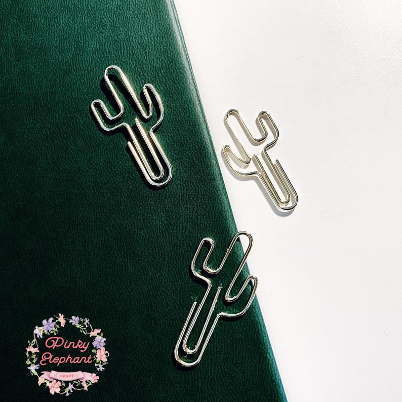 Three gold catcus-shaped paper clips are placing on a dark green leather notebook cover, in a white background