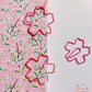 Two pink sakura-shaped paper clips are clamping on a pink green floral notebook cover, another one is placing on the right white background