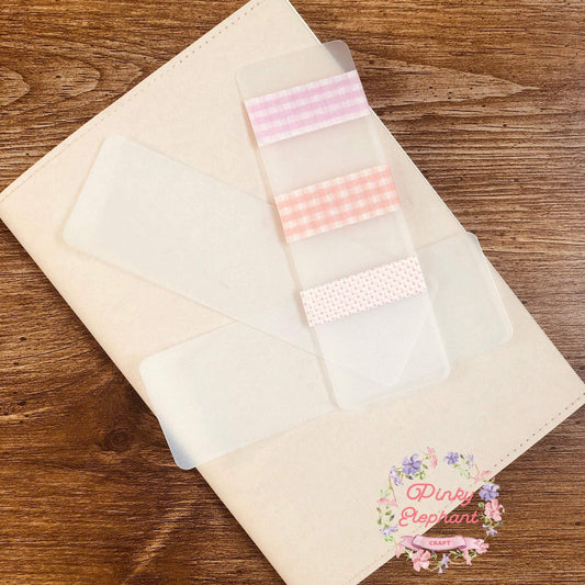 Three washi tape cards placing on a notebook, the top one decorated with three pink washi tapes, checkered and dotted, in a wooden backdrop